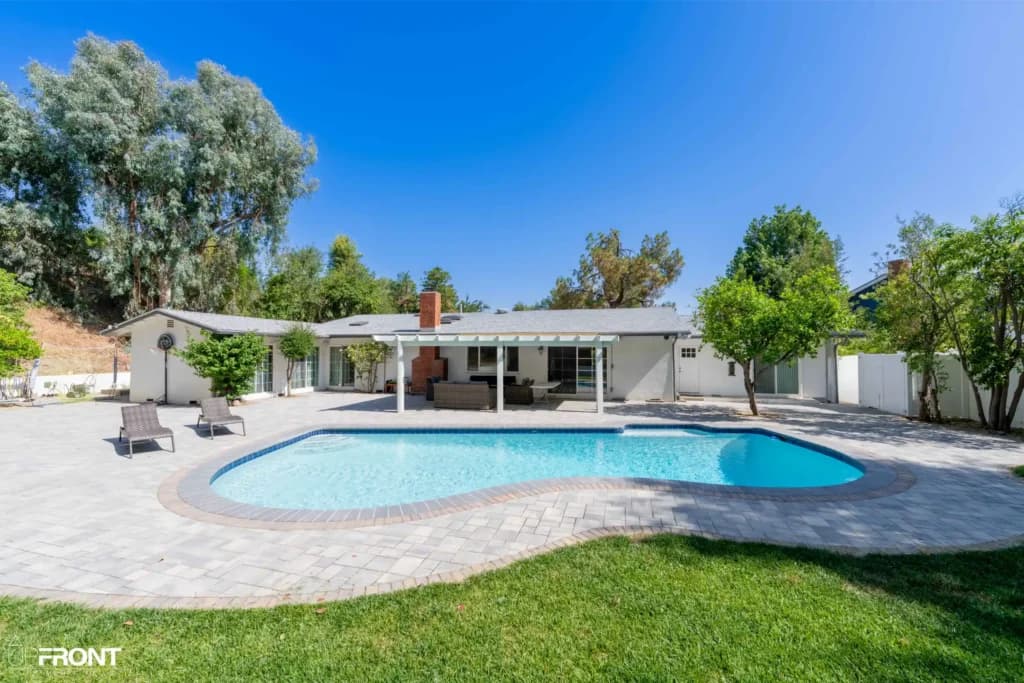 Resort-style backyard remodel in Tarzana, with a freeform pool, paver deck and louvered white pergola — photo 2 of 20